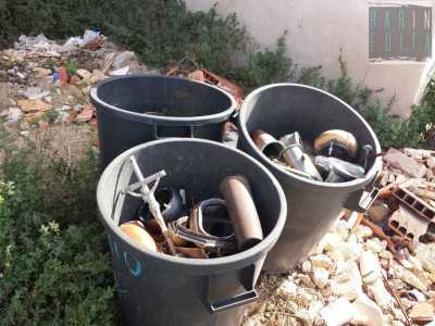 Tre bidoncini neri pieni di vasi per i fiori, crocifissi e lumini  
